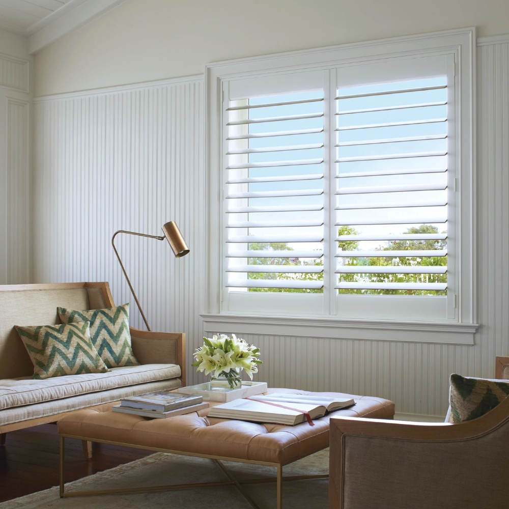 White composite shutters open in the living room with sofa, chairs and leather ottoman table