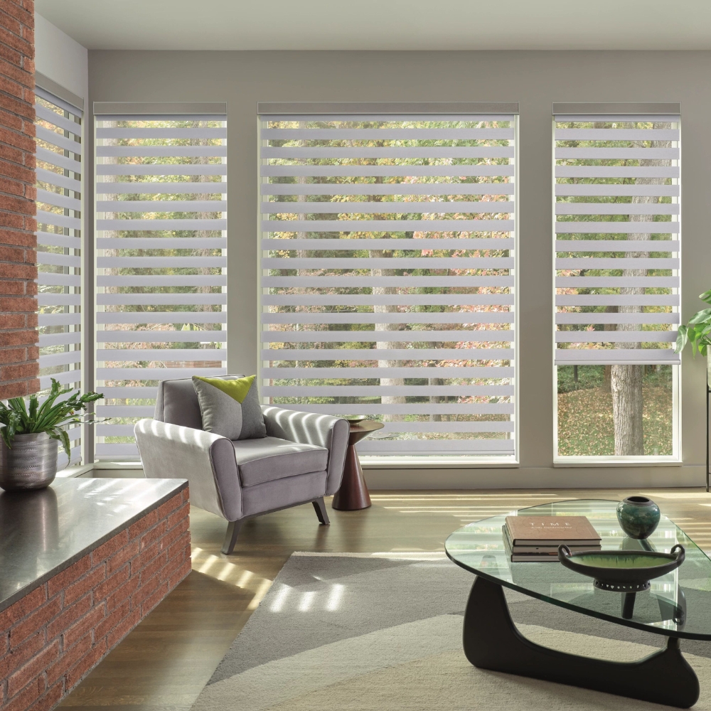 Living room with brick fireplace has sofa and chairs in front of designer banded shades with clearview sheers to the outside